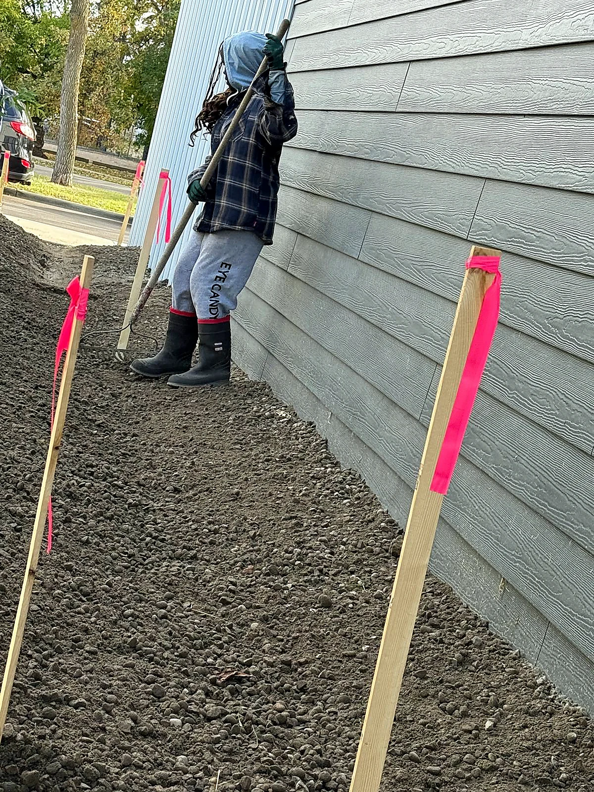 Worker fine grading soil beside a building exterior for drainage and finish preparation